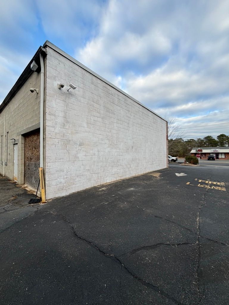 Exterior of a whitewashed brick building with a black asphalt parking lot under a cloudy sky.