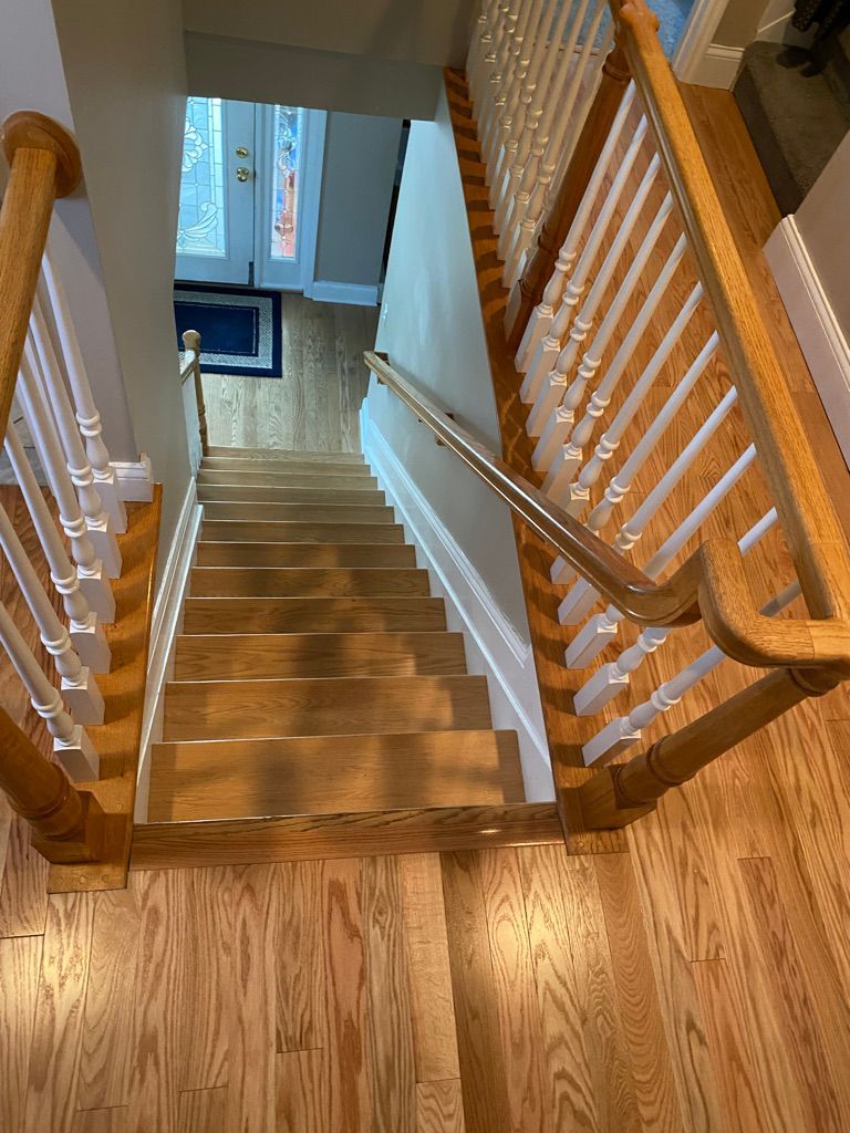 Wooden staircase viewed from above, leading down towards a door, with wood flooring on both sides.