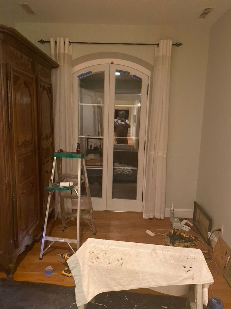 Room with white doors, light curtains on a rod, a tall wooden armoire, and a step ladder.