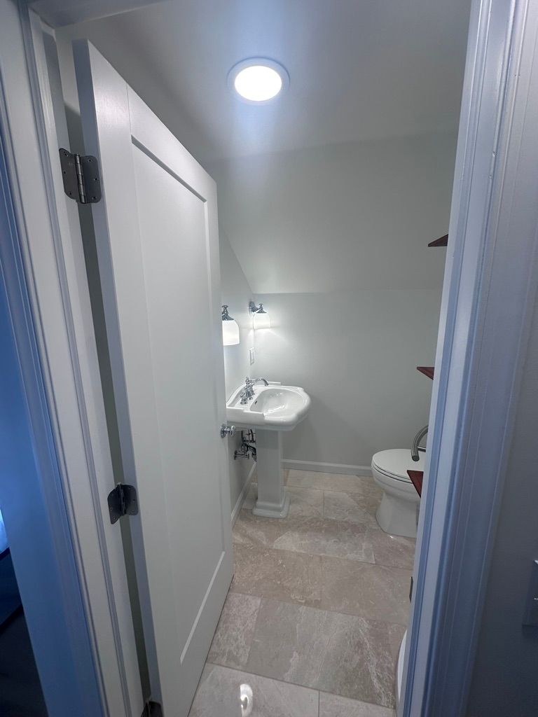 Small bathroom with pedestal sink, toilet, and open door. Light gray walls and flooring.