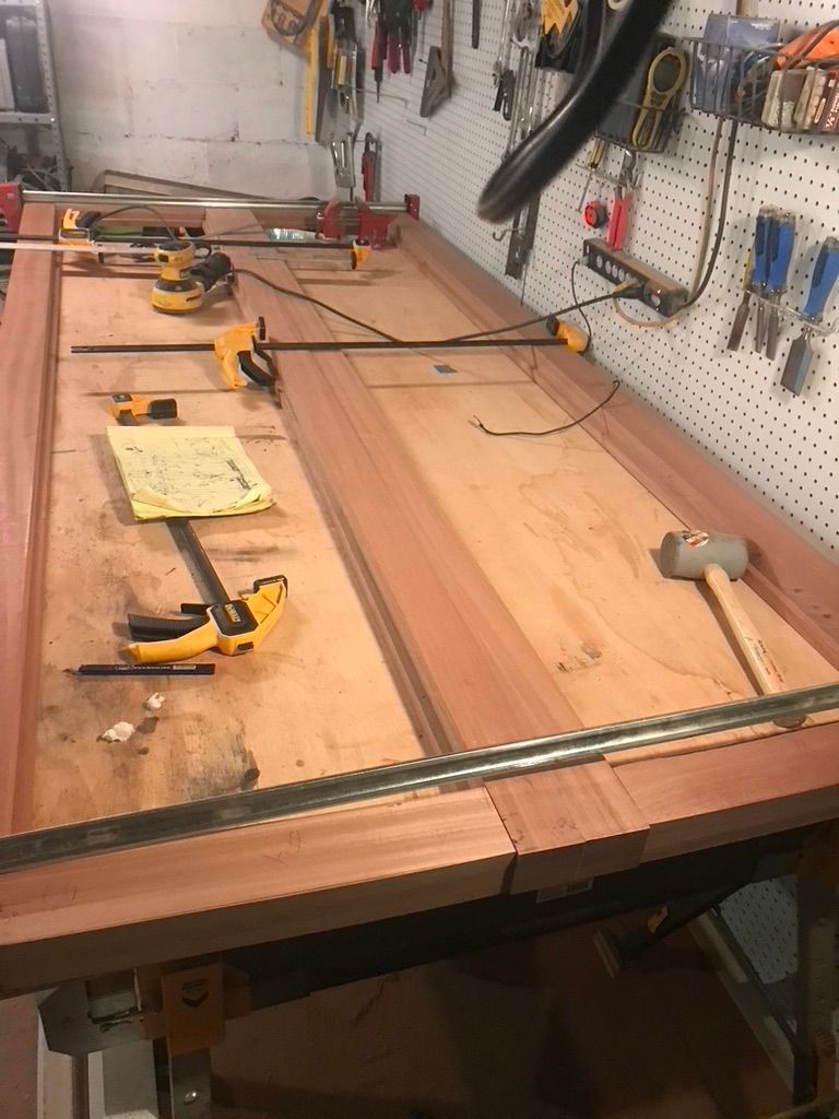 Wooden door being assembled with clamps in a workshop, tools hanging in the background.