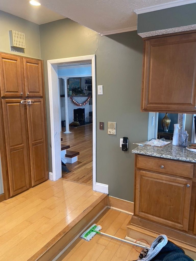 Kitchen with wooden cabinets, light-colored floor, doorway to another room, and a small step.