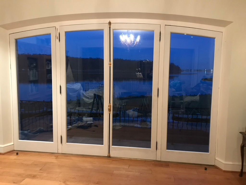 Four-panel glass doors with a white frame and curved top, overlooking water. A chandelier is visible inside.