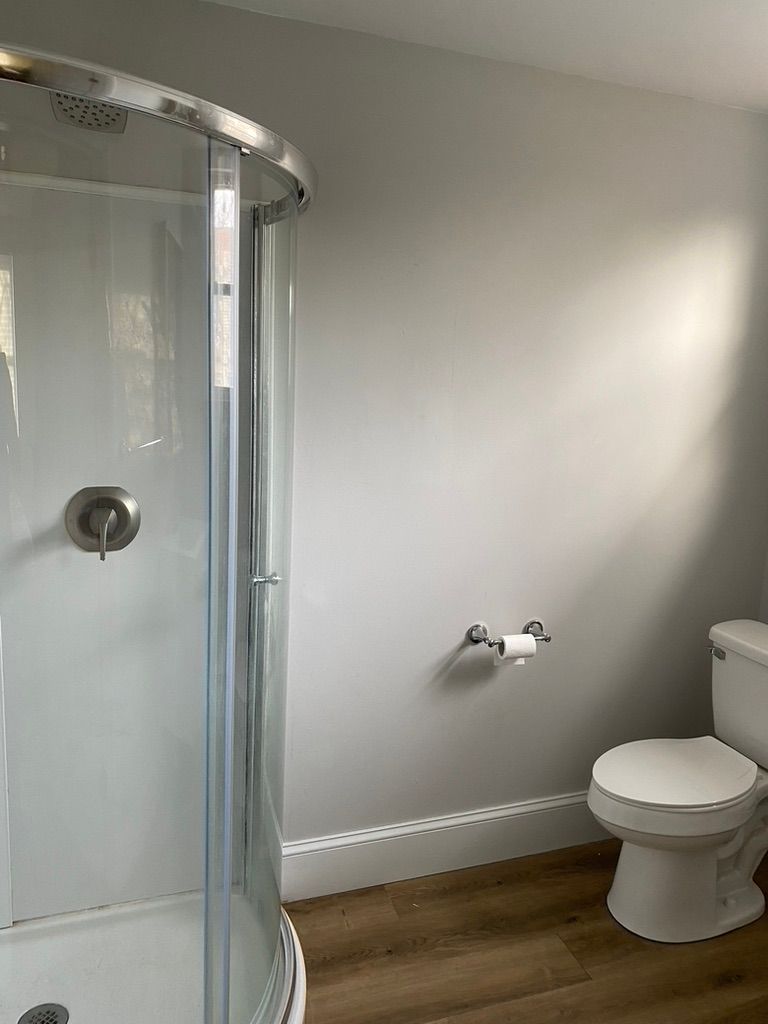 Bathroom with a curved glass shower, toilet, and gray walls, with wooden floors.