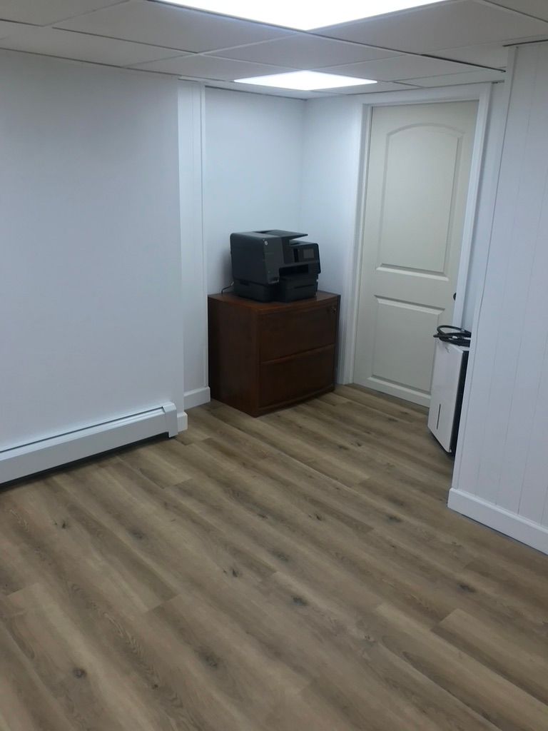 Empty room with wood-look floor, white walls, door, and a printer on a wooden cabinet.