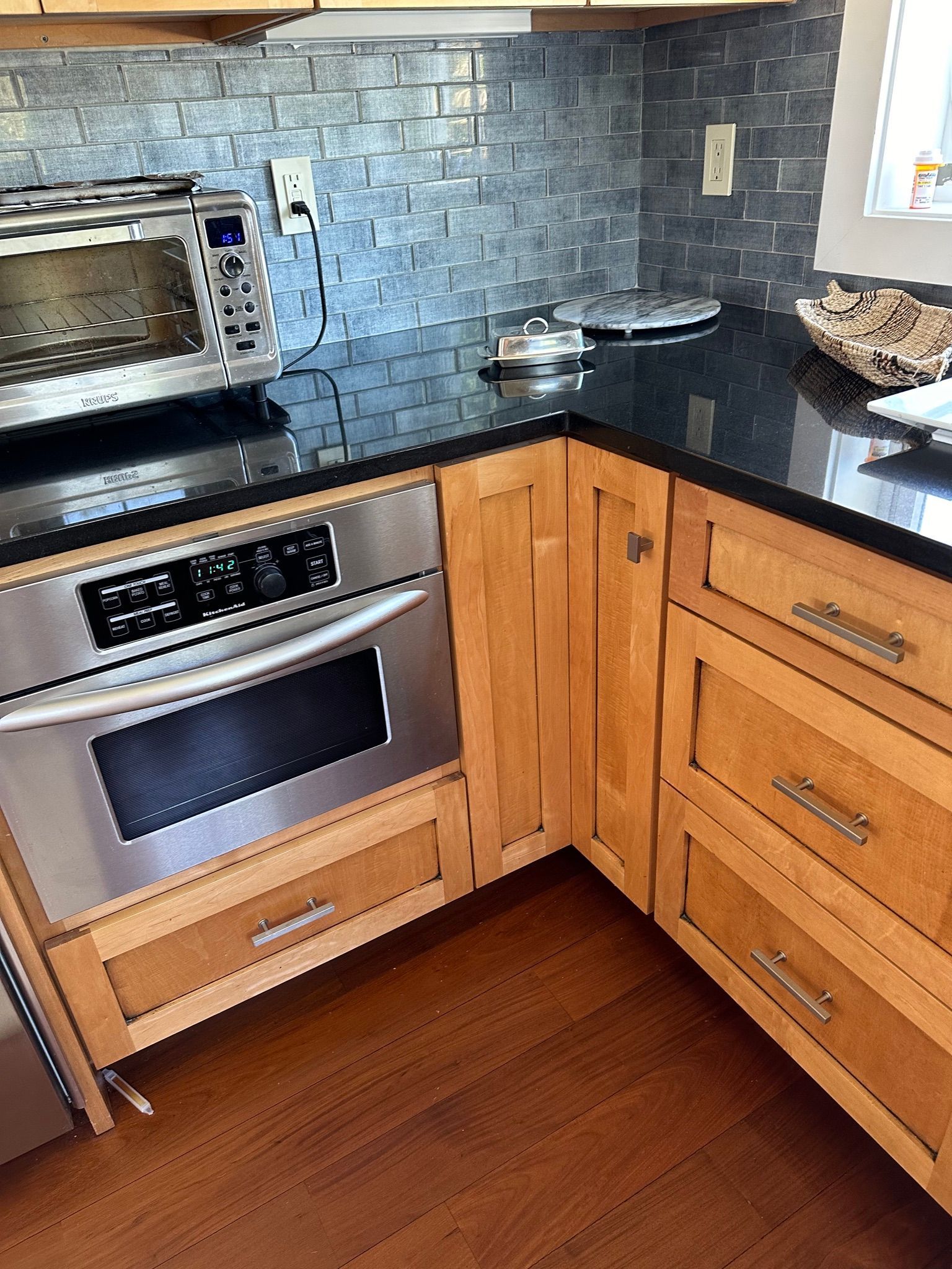 Kitchen corner with stainless steel oven, wooden cabinets, and black countertop.