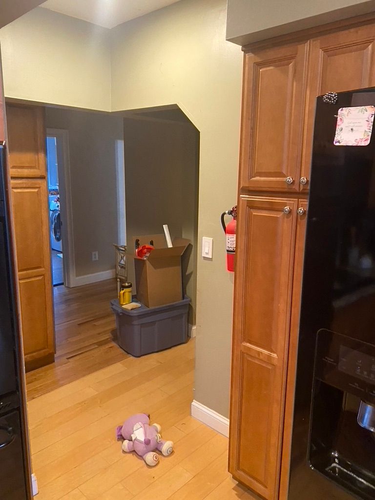 Kitchen with wood cabinets and flooring, doorway to hallway, box and toy on floor.