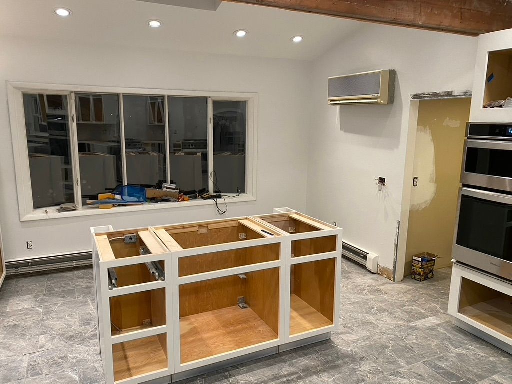 Kitchen renovation: partially installed white cabinets, unfinished floors, window, oven, air conditioner.