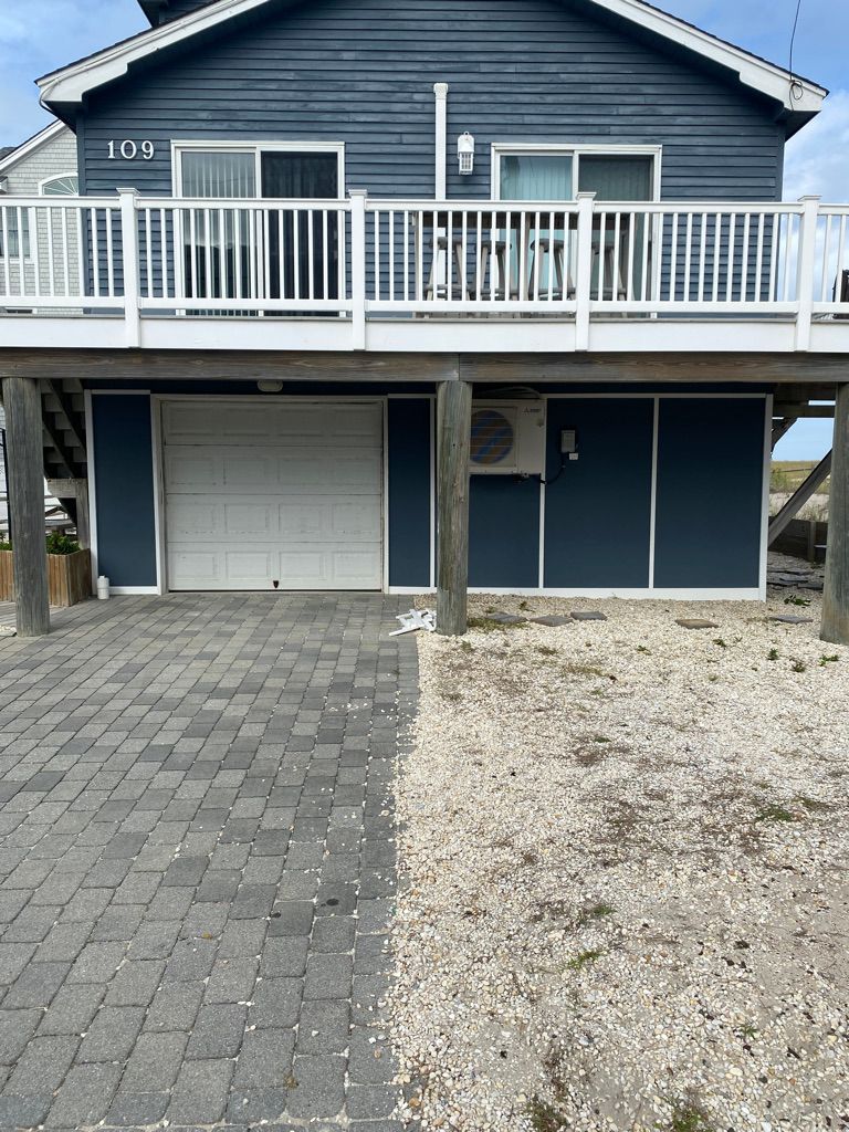 Blue beach house with a white deck, garage, and paved driveway.