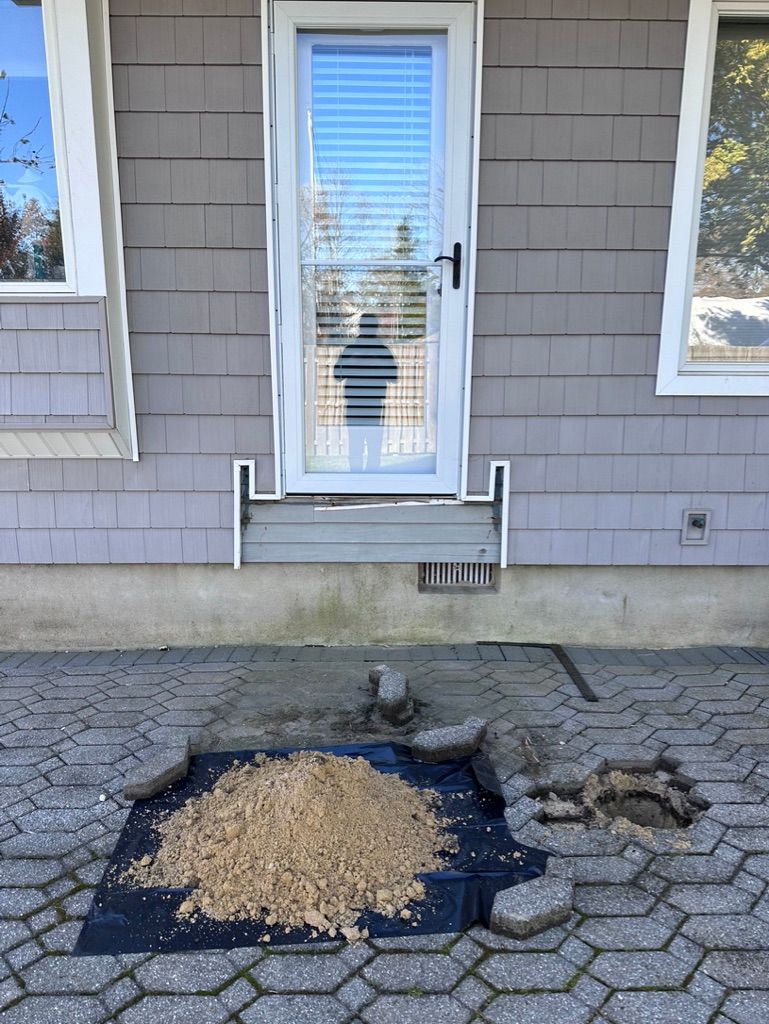 Doorway with damaged pavers, sand pile, and weed barrier.