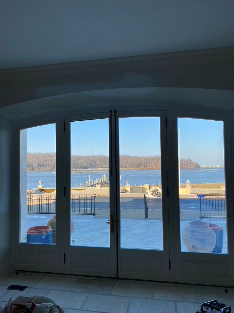 French doors offer a view of a waterfront with trees and a dock.