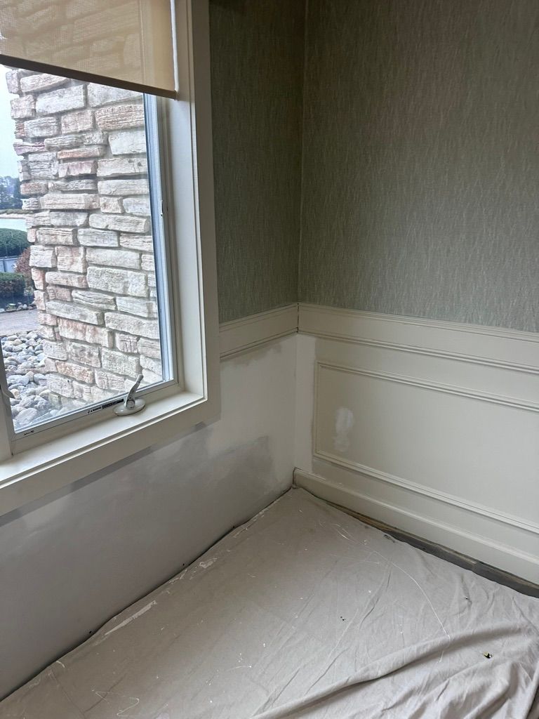 Corner room with window and decorative trim. Stone exterior visible through window. Painting in progress.