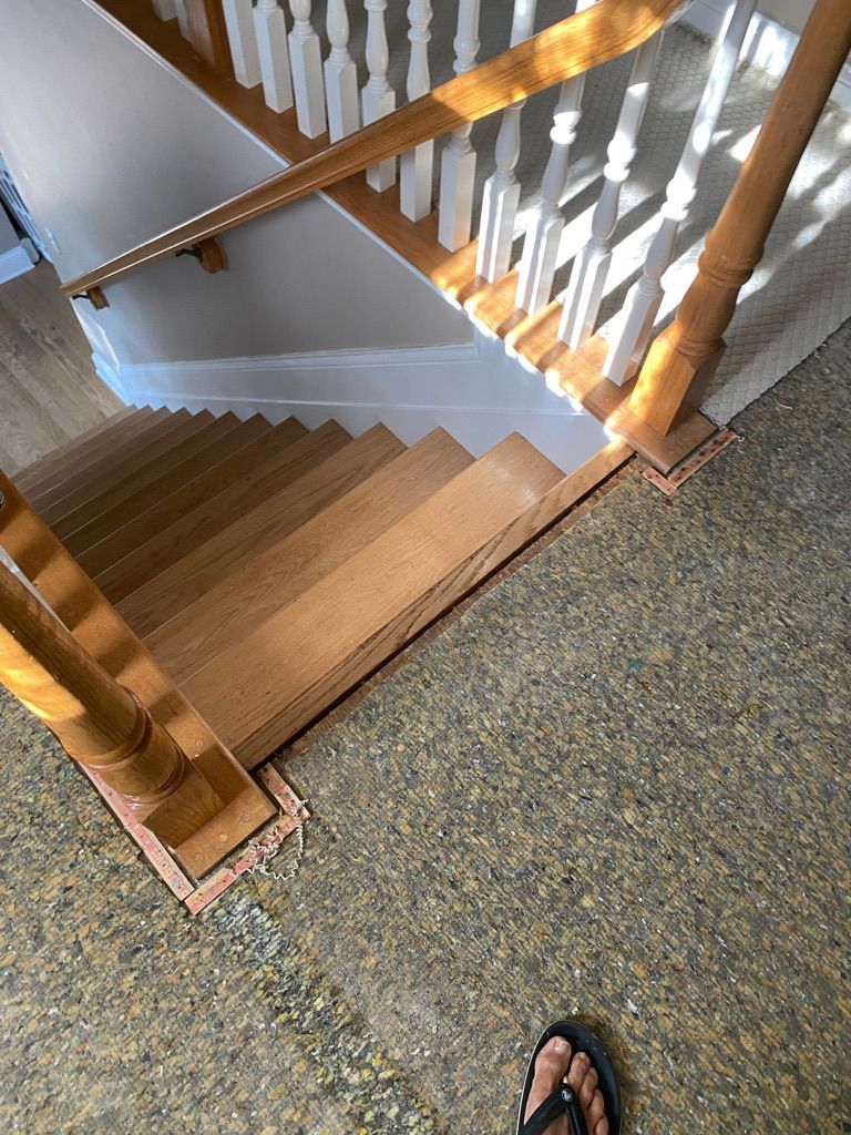 Wooden staircase viewed from above, with brown steps, white banister, and speckled floor.