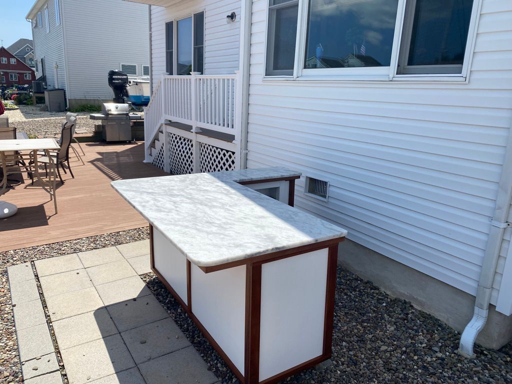 Outdoor bar with white counter, wooden frame, and white siding on a sunny day.