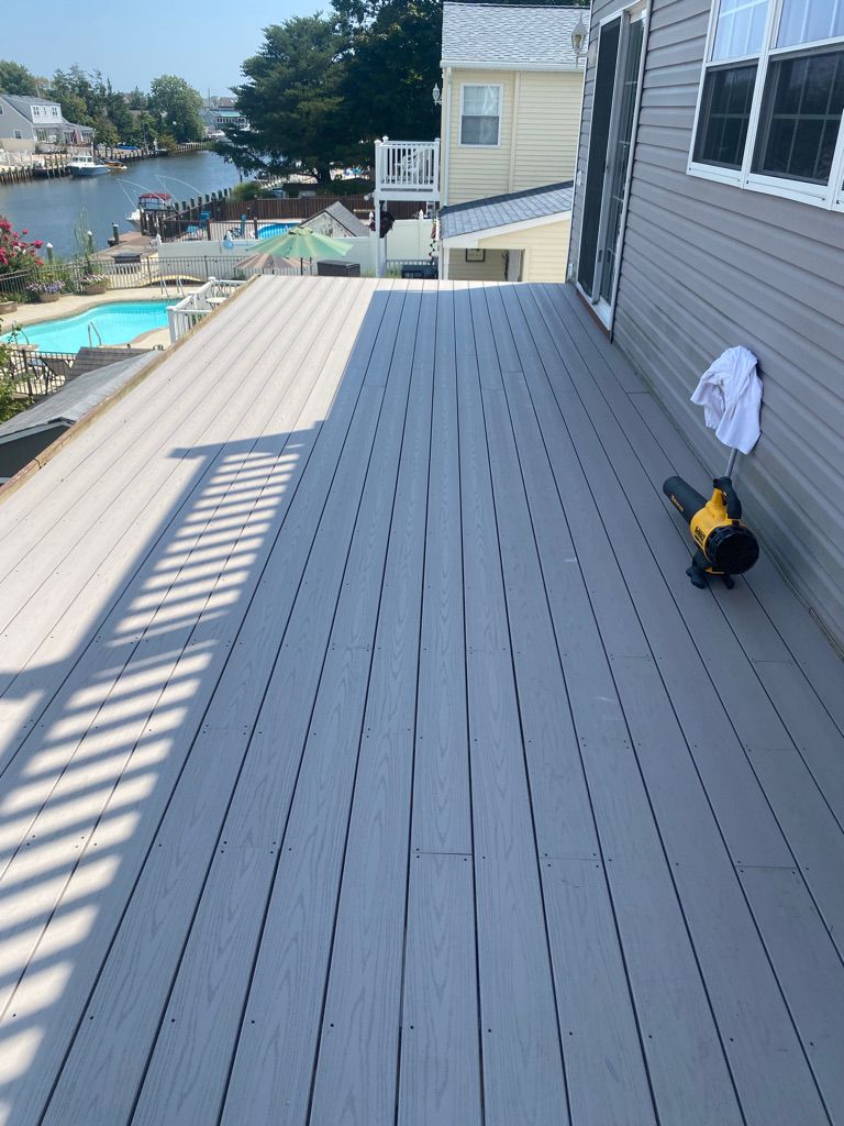 Wide, gray composite deck with a view of a pool and waterway. A leaf blower and rag hang on the house's side.