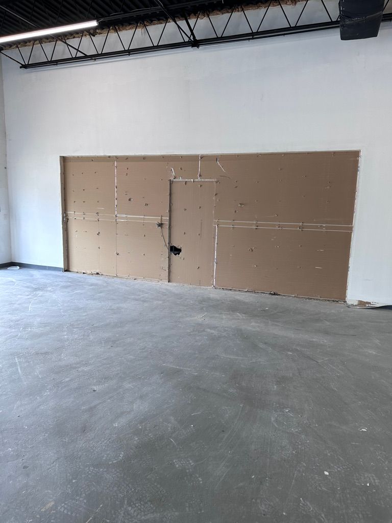 Interior of a room with unfinished drywall section in a white-walled space with a gray floor.