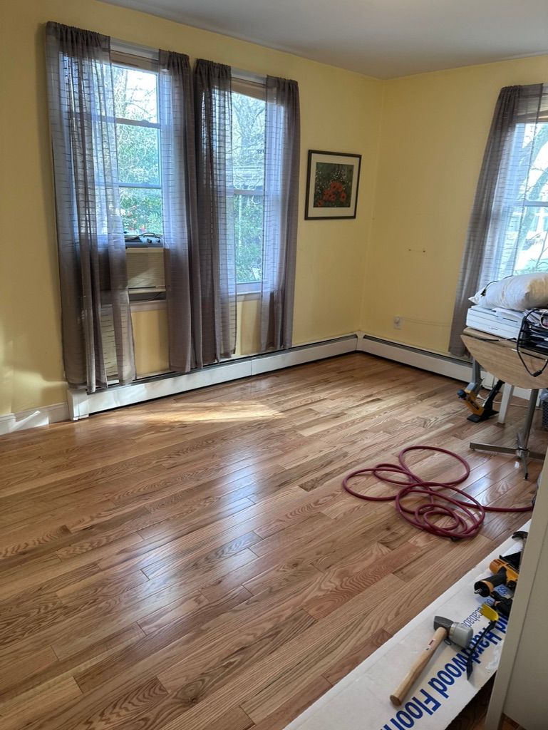 Hardwood floor installation in a room with windows and yellow walls; tools on the floor.