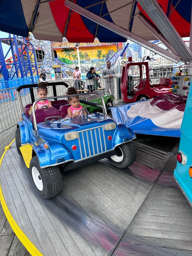 Two children in a blue Jeep ride on a carousel at an amusement park.
