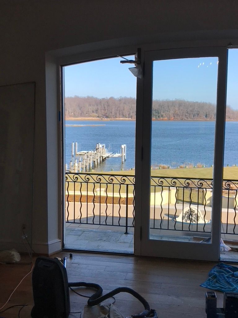 Open glass doors reveal a pier over a blue body of water, a shoreline with trees, and an interior with equipment.