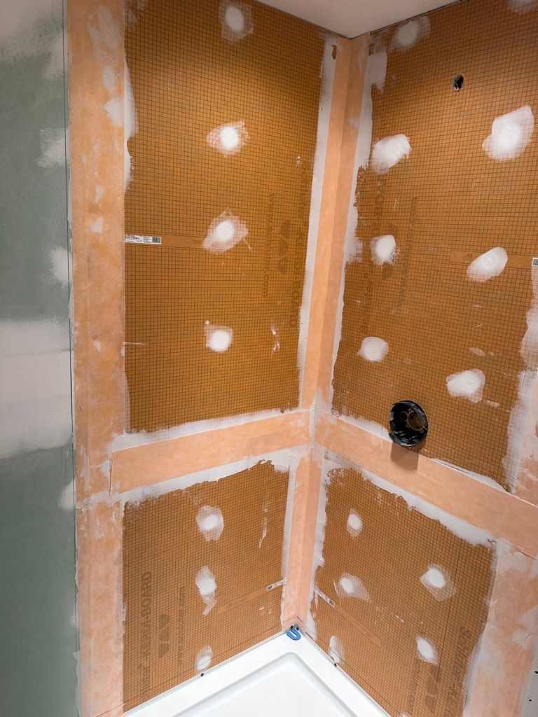 Bathroom wall under construction, showing orange membrane with white sealant and studs visible.
