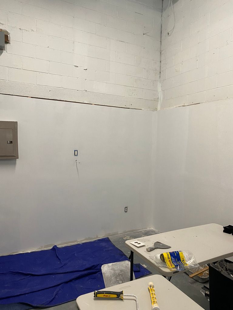 Empty white room with electrical box, tables, and blue tarp on floor.