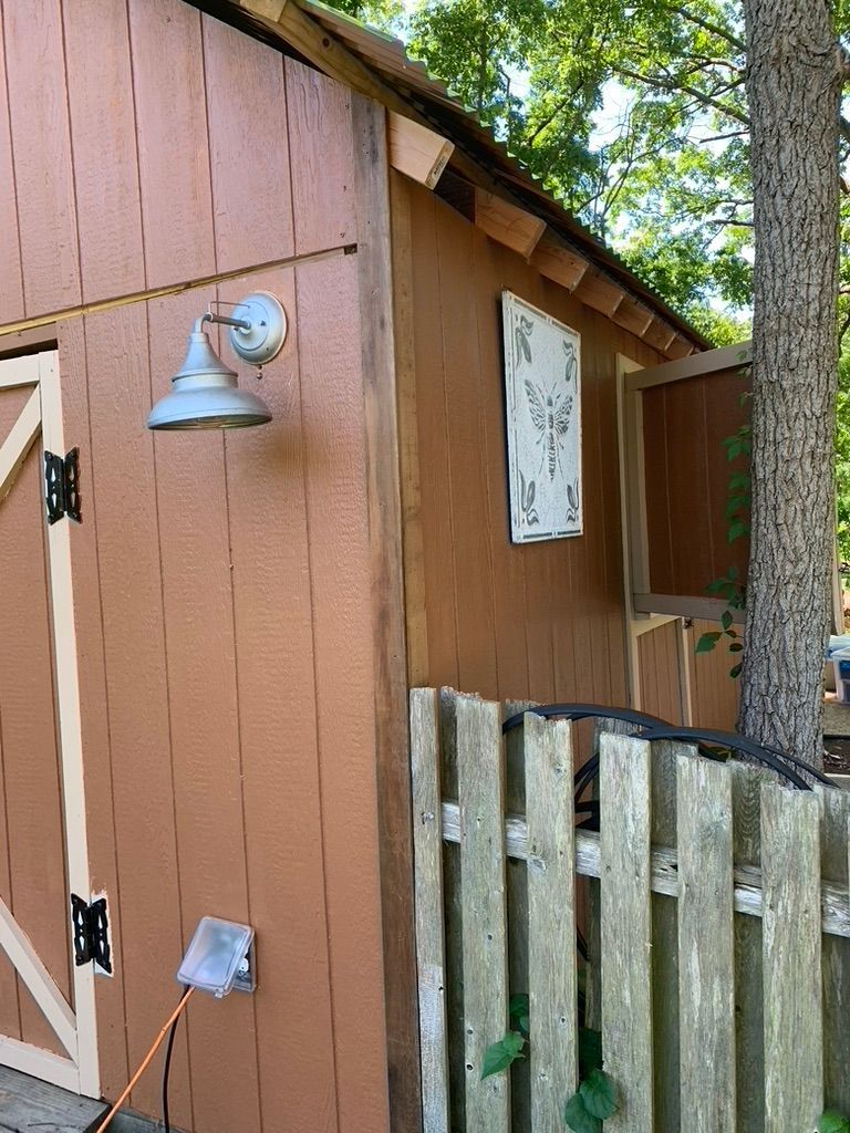 Brown shed with a light fixture, a window, and a wooden fence.