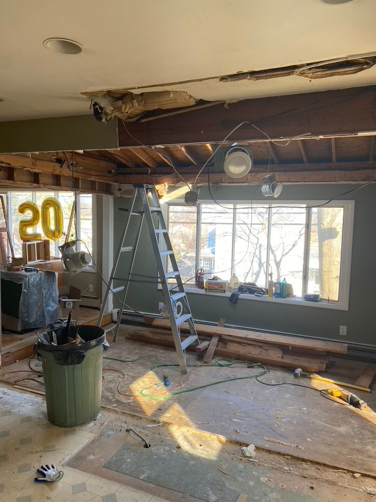Interior undergoing renovation; exposed beams, ladder, debris, and partial window view. 