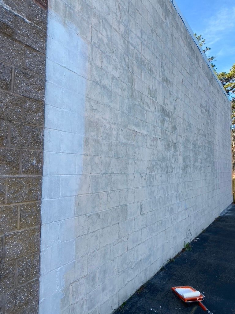 Concrete block wall being painted white, with a roller on the ground.