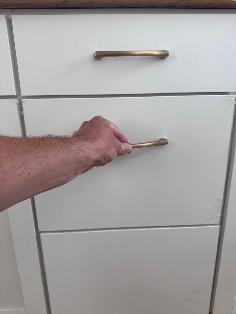 Person opening a white kitchen cabinet drawer with a gold handle.