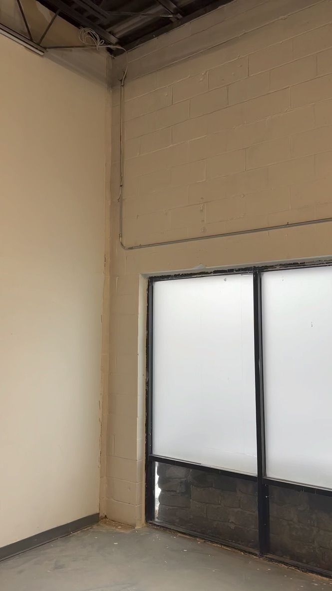 Interior of a room with a white wall and a glass door with frosted film. Concrete floor.