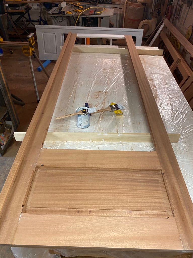 Wooden door frame under construction in workshop. Clamps and adhesive are visible.