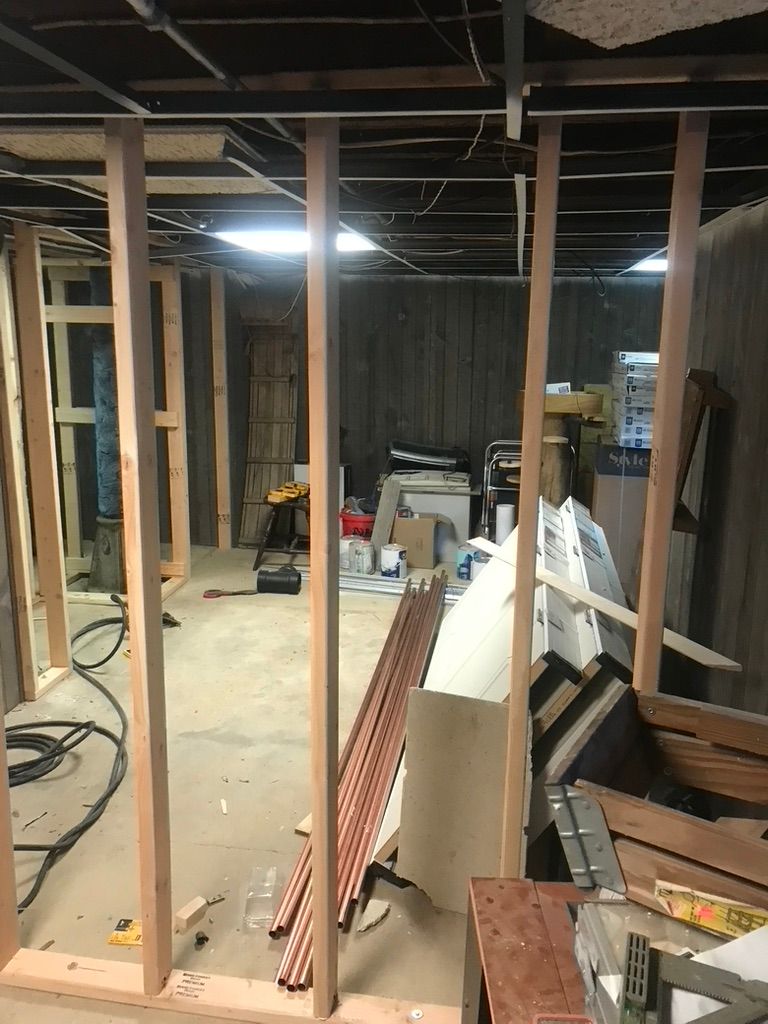 Basement under construction, framing a wall. Copper pipes and tools are scattered on the floor.