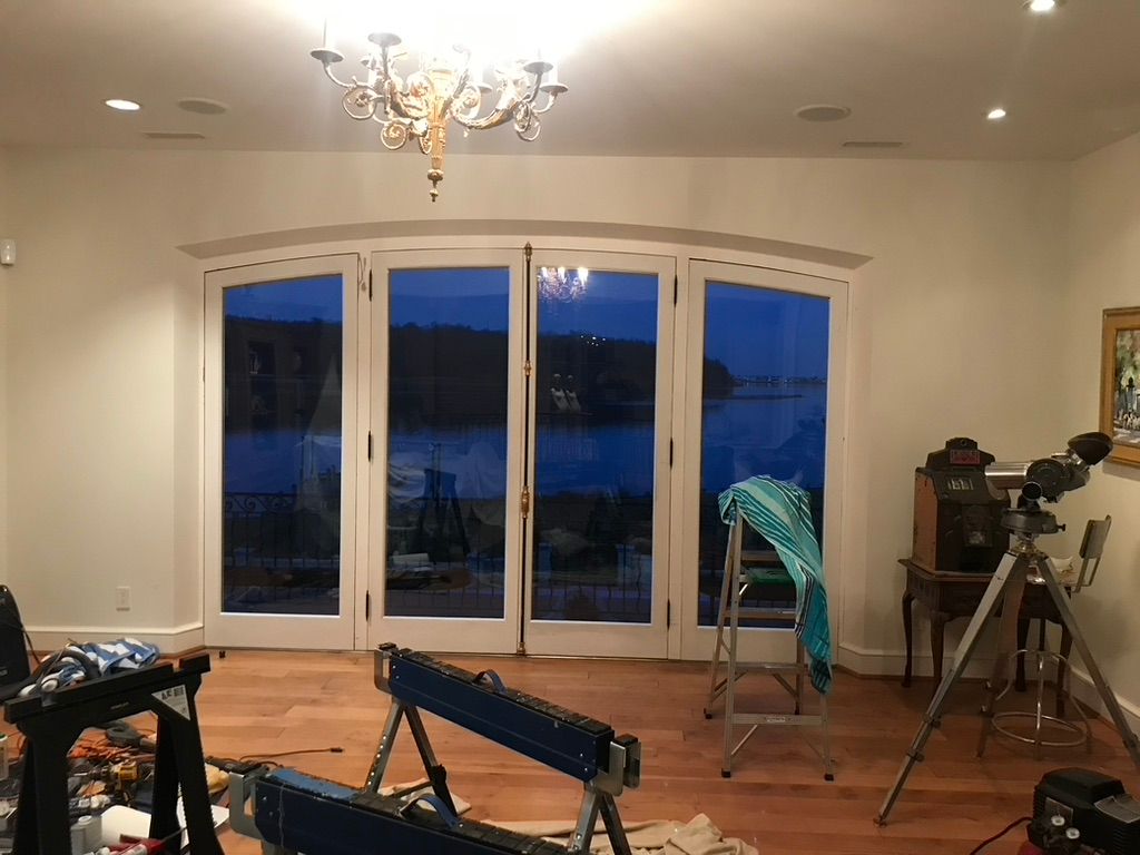 Room with large arched doors overlooking a body of water at dusk. Includes chandelier, telescope, and various objects.