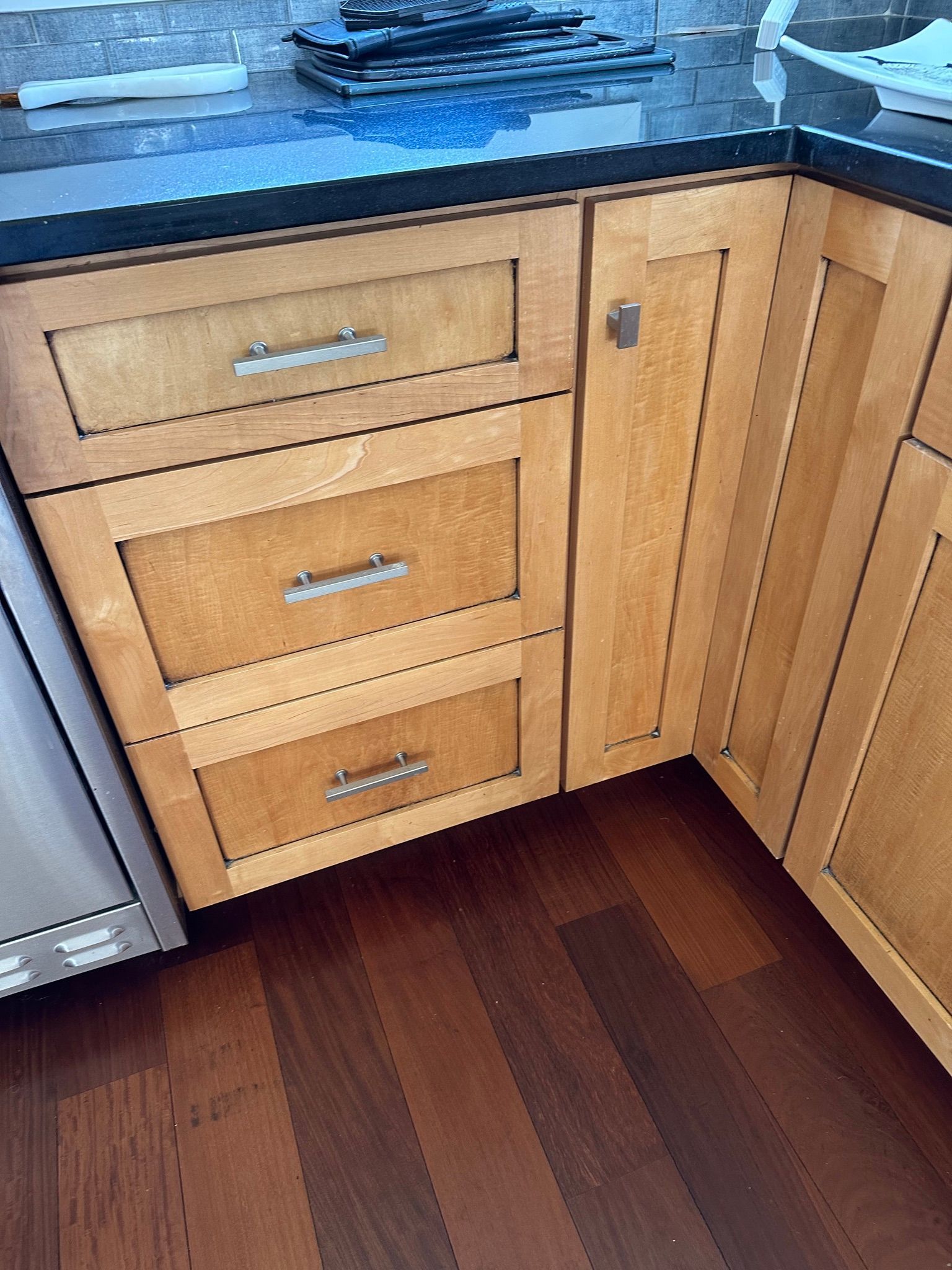 Wooden kitchen cabinets with drawers and a door, next to a countertop and dark wood floor.