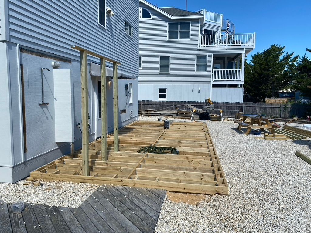 Wooden deck under construction next to a house with gravel ground.