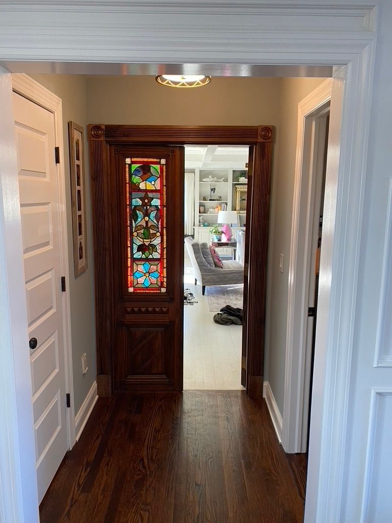 Hallway with stained glass door, dark wood flooring, and white trim.