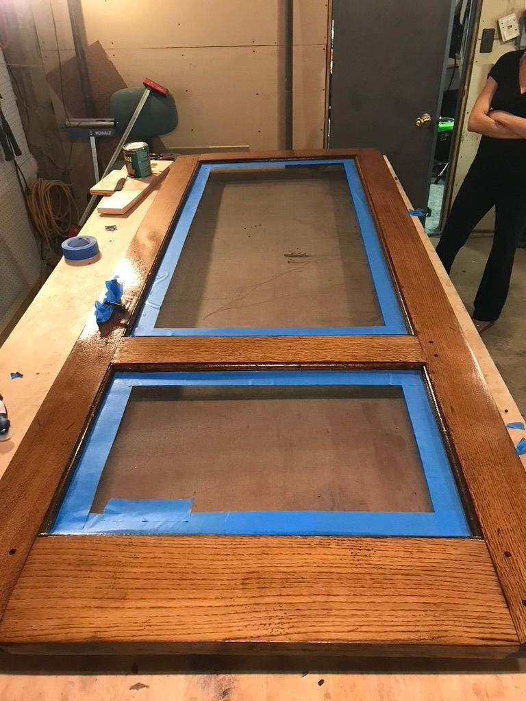 Wooden door frame with two rectangular glass panes, taped with blue painter's tape, on a workbench.