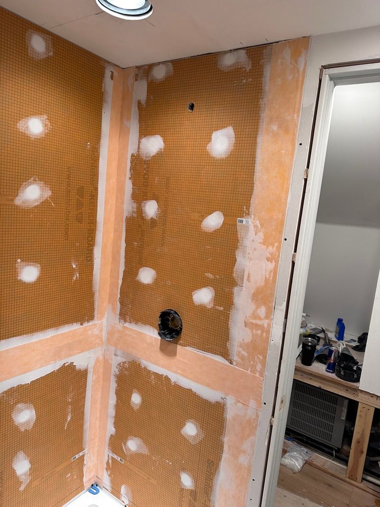 Shower stall construction in progress with orange membrane, cement board, and patched areas.