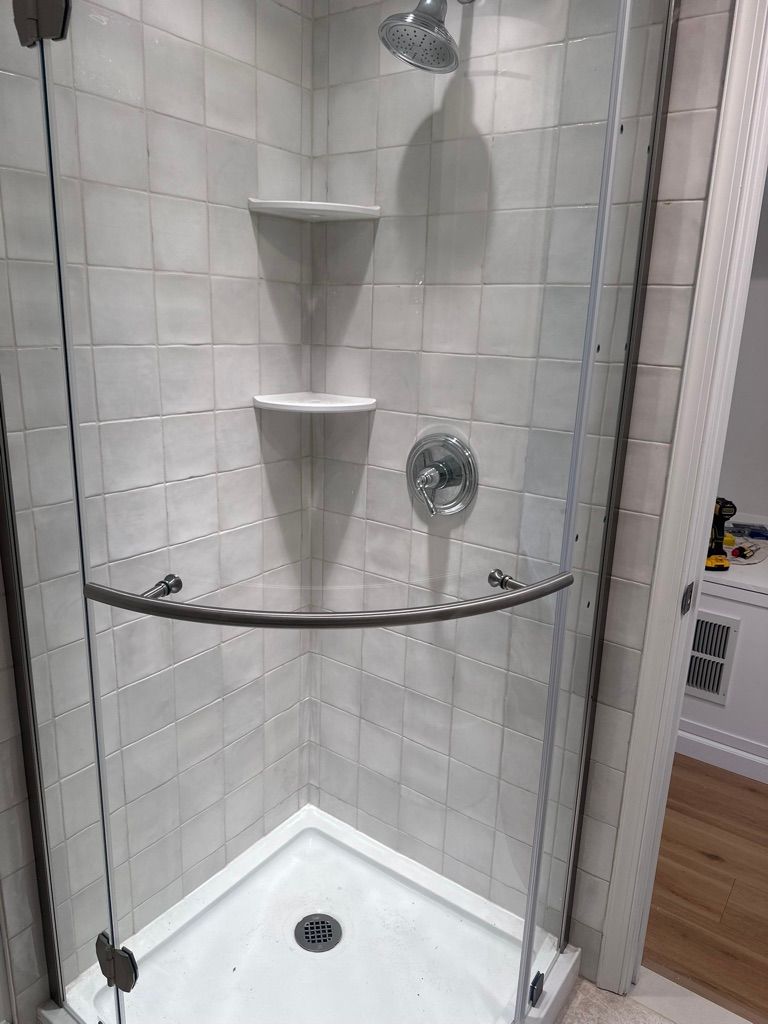 Corner shower with glass doors, white tiled walls, shelves, and showerhead.