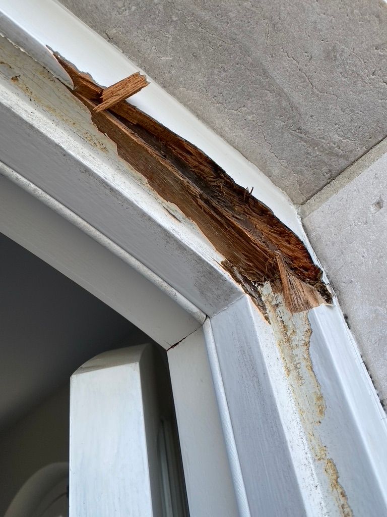 Damaged white door frame with exposed, decaying wood and a concrete overhang.