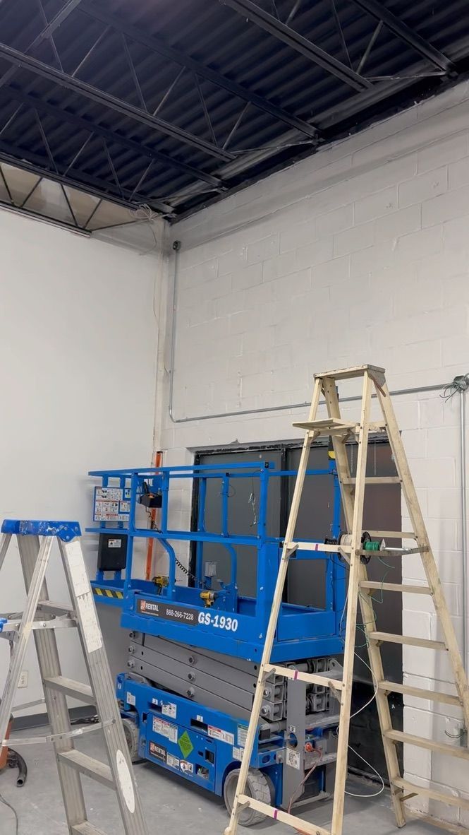 Blue lift and ladders inside a room with a high ceiling, electrical work in progress.