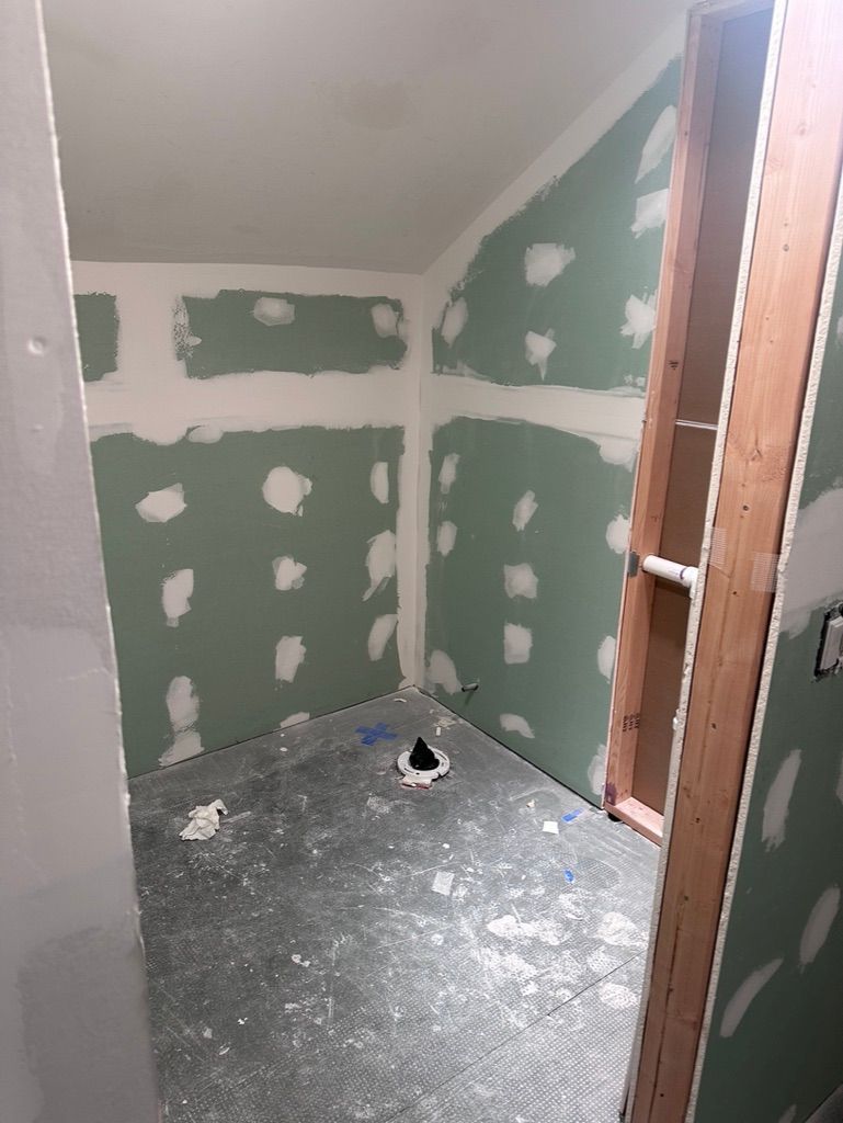 Small bathroom under construction; green drywall with joint compound; unfinished floor and wood framing.