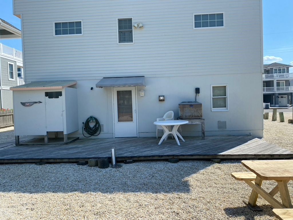 Back of a two-story light gray house with a small patio, a shed, and a picnic table on a gravel lot.
