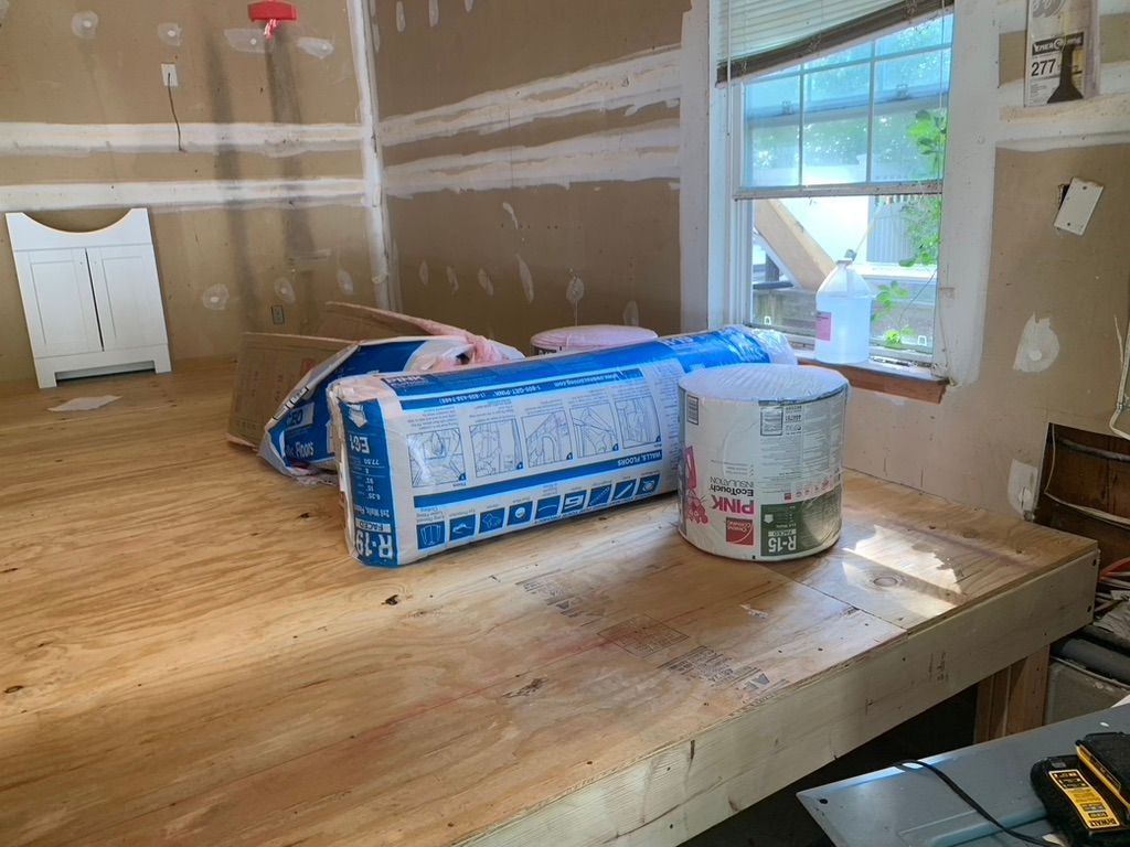 Interior view of a workspace with insulation rolls on a wooden surface, near a window.