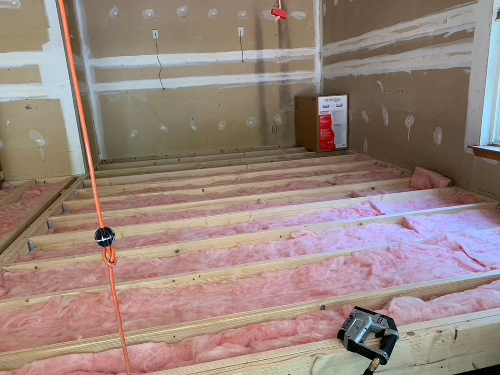 Interior construction: pink insulation between floor joists, drywall walls, cardboard box.