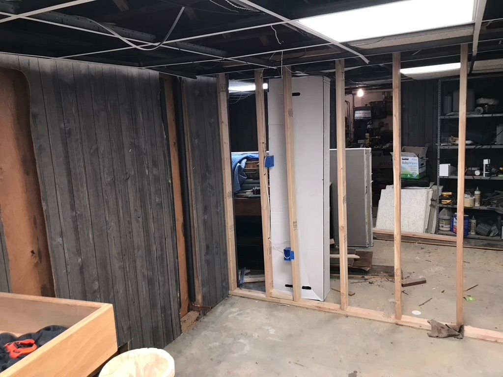 Basement renovation: Framing for a new wall, exposed studs, unfinished space, concrete floor, dim lighting.