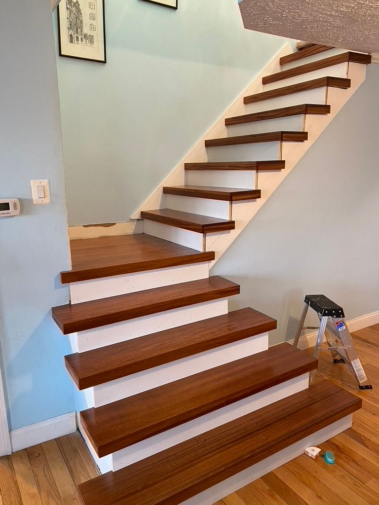 Wooden staircase with brown treads and white risers, ascending against a light blue wall.