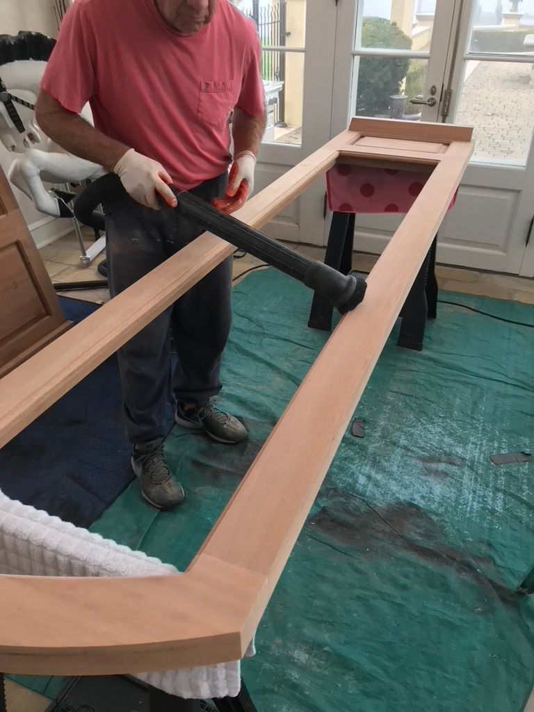 Man using a vacuum to clean a wooden door frame, indoors, near windows and a tarp.