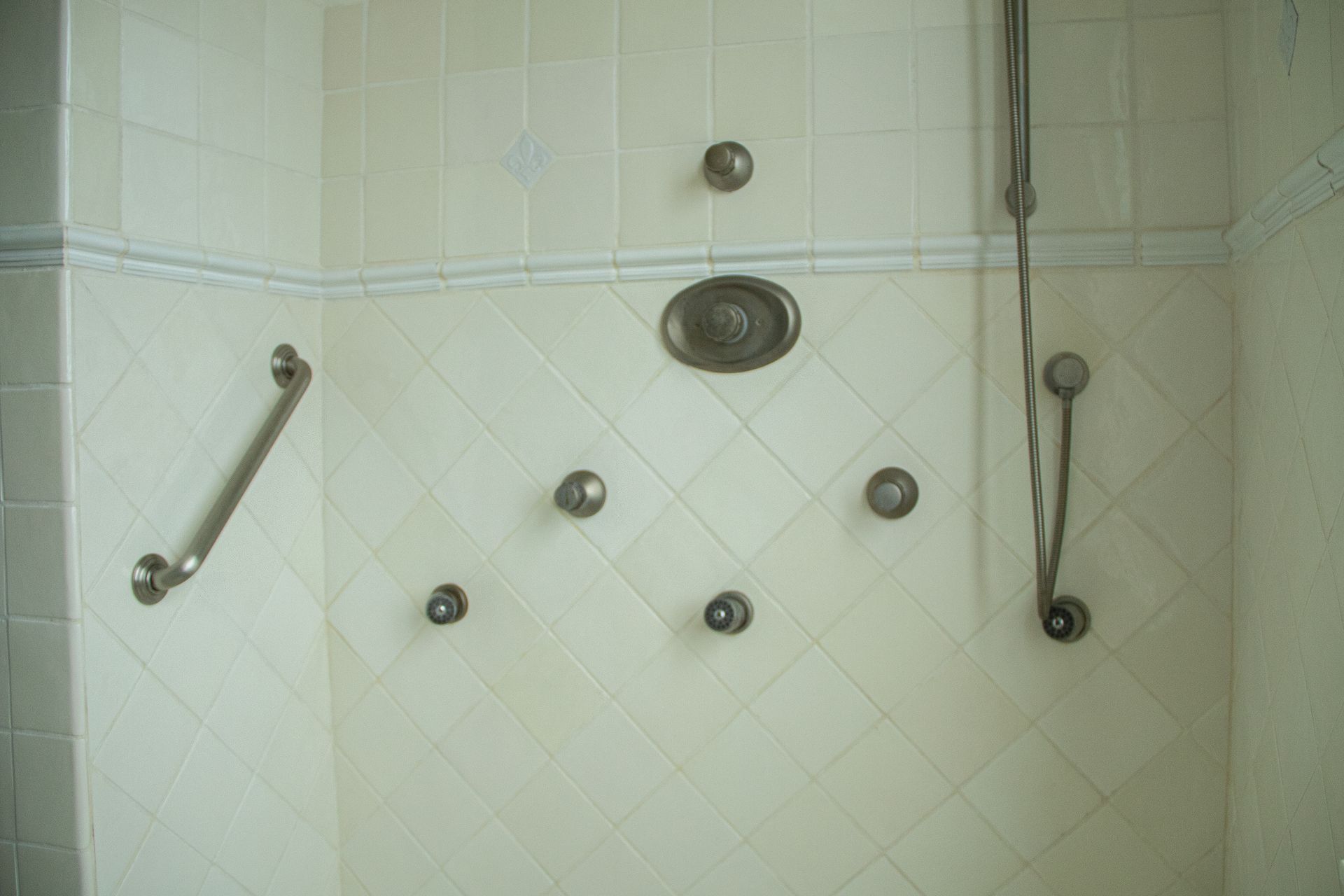 White tiled shower with multiple body jets, overhead showerhead, and a grab bar.