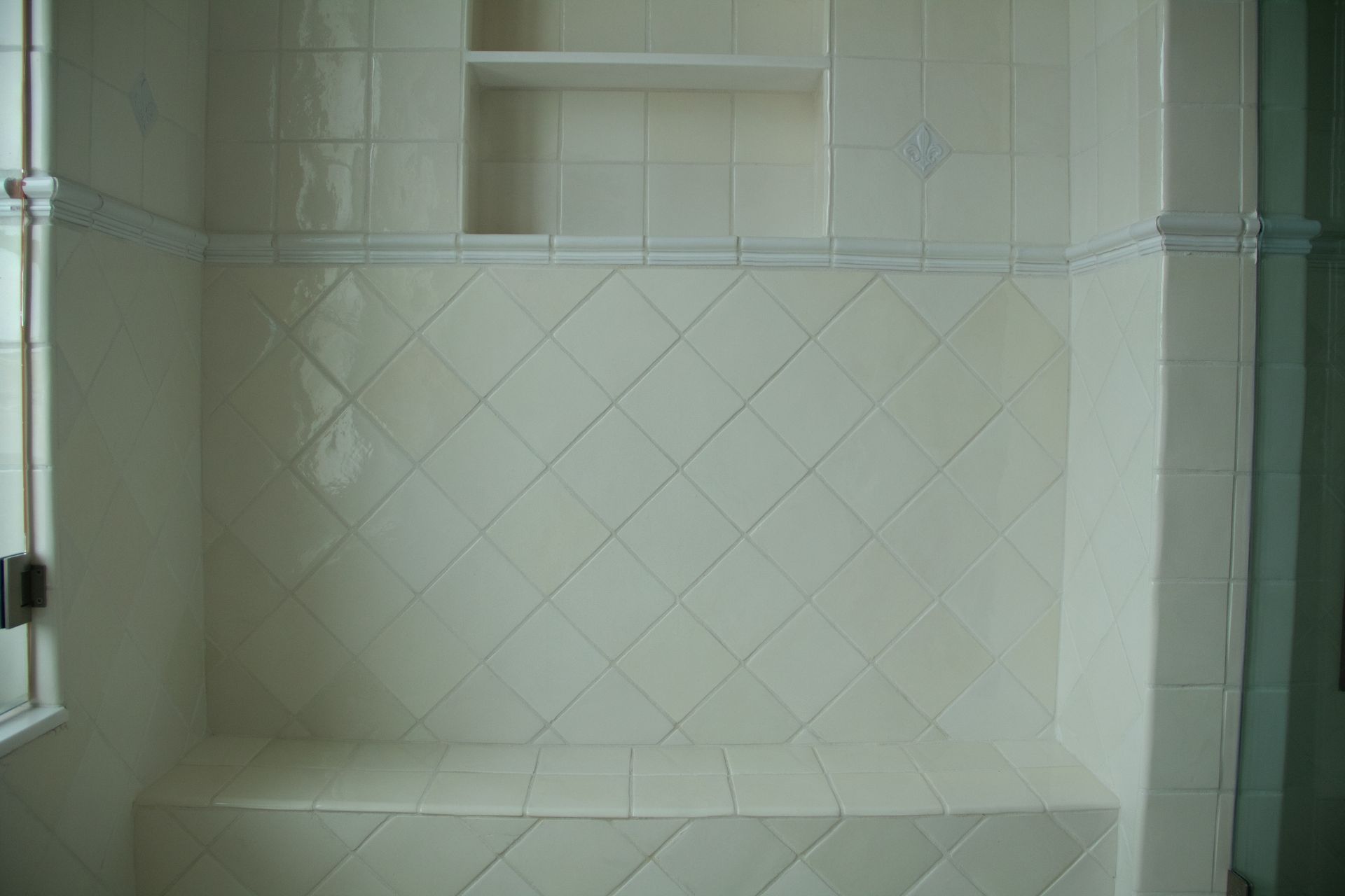 Bathroom shower with white, diamond-patterned tiles, built-in bench, and a small shelf.